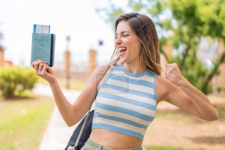 Téléchargez les photos : Jeune jolie femme tenant un passeport en plein air célébrant une victoire - en image libre de droit