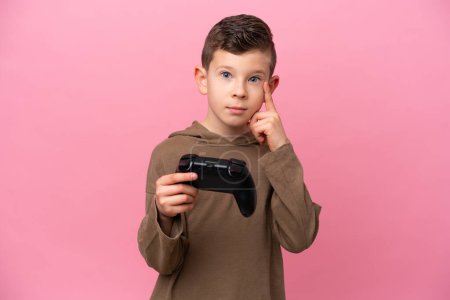 Téléchargez les photos : Petit garçon caucasien jouant avec un contrôleur de jeu vidéo isolé sur fond rose pensant une idée - en image libre de droit