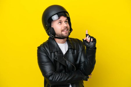 Foto de Joven hombre caucásico con casco de moto aislado sobre fondo amarillo apuntando a una gran idea - Imagen libre de derechos