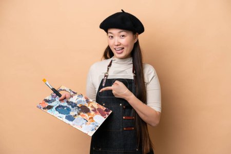 Téléchargez les photos : Young Chinese painter woman isolated on beige background pointing to the side to present a product - en image libre de droit
