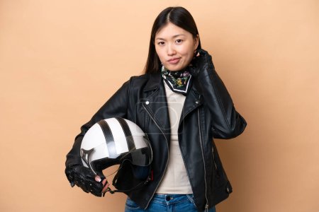Foto de Joven mujer china con un casco de motocicleta aislado sobre fondo beige que tiene dudas - Imagen libre de derechos