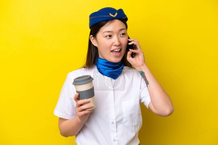 Photo for Airplane Chinese woman stewardess isolated on yellow background keeping a conversation with the mobile phone - Royalty Free Image