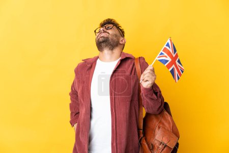 Foto de Hombre caucásico sosteniendo una bandera del Reino Unido aislado sobre fondo amarillo que sufre de dolor de espalda por haber hecho un esfuerzo - Imagen libre de derechos