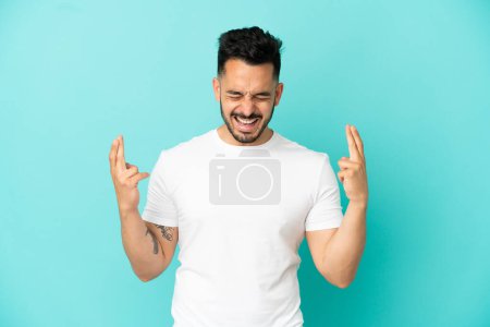 Photo for Young caucasian man isolated on blue background with fingers crossing - Royalty Free Image