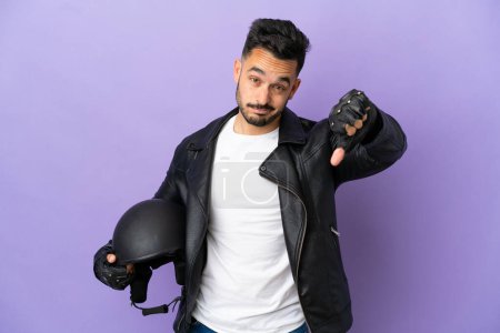Téléchargez les photos : Jeune homme avec un casque de moto isolé sur fond violet montrant pouce vers le bas avec une expression négative - en image libre de droit