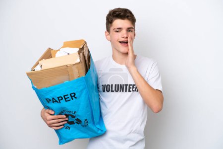 Teenager Russian man holding a recycling bag full of paper to recycle isolated on white background shouting with mouth wide open