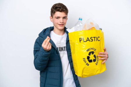 Téléchargez les photos : Adolescent russe tenant un sac rempli de bouteilles en plastique à recycler sur fond blanc faisant geste d'argent - en image libre de droit