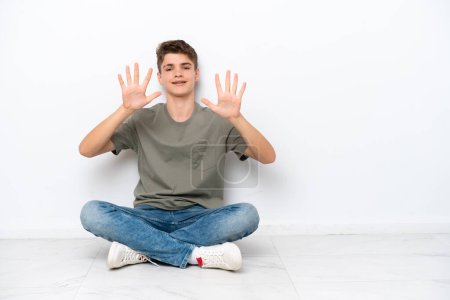 Foto de Adolescente ruso hombre sentado en el suelo aislado sobre fondo blanco contando diez con los dedos - Imagen libre de derechos