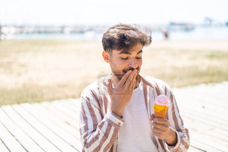 Téléchargez les photos : Bel homme arabe avec une crème glacée cornet à l'extérieur avec une expression faciale surprise et choquée - en image libre de droit