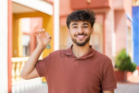 Téléchargez les photos : Jeune homme beau arabe à l'extérieur tenant les clés de la maison avec une expression heureuse - en image libre de droit