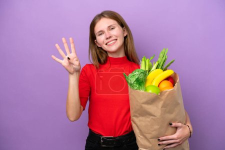 Photo for Young English woman holding a grocery shopping bag isolated on purple background happy and counting four with fingers - Royalty Free Image