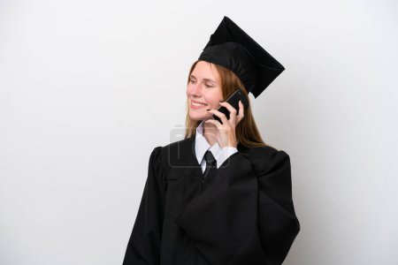 Foto de Joven graduada universitaria inglesa aislada sobre fondo blanco manteniendo una conversación con el teléfono móvil con alguien - Imagen libre de derechos