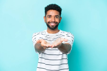 Photo for Young Brazilian man isolated on blue background holding copyspace imaginary on the palm to insert an ad - Royalty Free Image