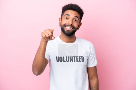 Young volunteer man isolated on pink background surprised and pointing front