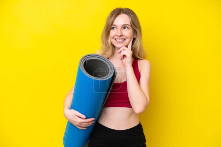 Photo for Young sport caucasian woman going to yoga classes while holding a mat isolated on yellow background thinking an idea while looking up - Royalty Free Image