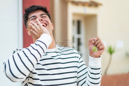Foto de Joven hombre hispano al aire libre sosteniendo las llaves del hogar con expresión feliz - Imagen libre de derechos