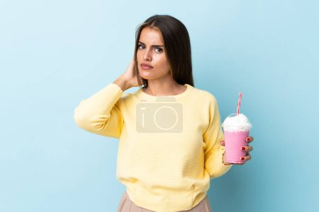 Téléchargez les photos : Jeune femme uruguayenne avec milkshake fraise isolé sur fond bleu ayant des doutes - en image libre de droit