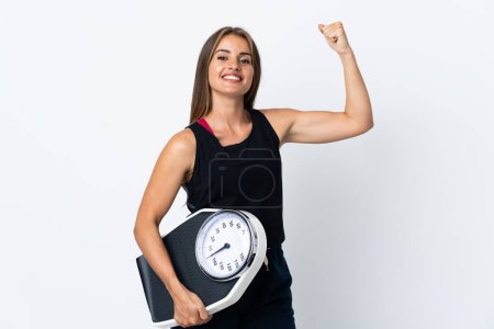 Photo for Young Uruguayan woman isolated on white background holding a weighing machine and doing strong gesture - Royalty Free Image