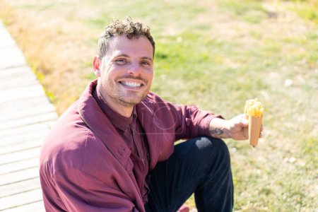 Photo for Young caucasian man holding fried chips at outdoors smiling a lot - Royalty Free Image