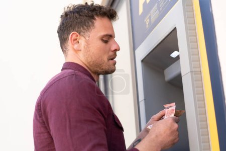 Photo for Young caucasian man at outdoors using an ATM - Royalty Free Image