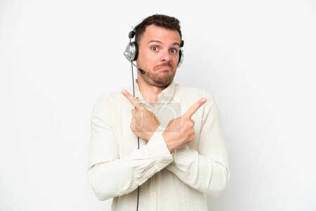 Photo for Telemarketer caucasian man working with a headset isolated on white background pointing to the laterals having doubts - Royalty Free Image