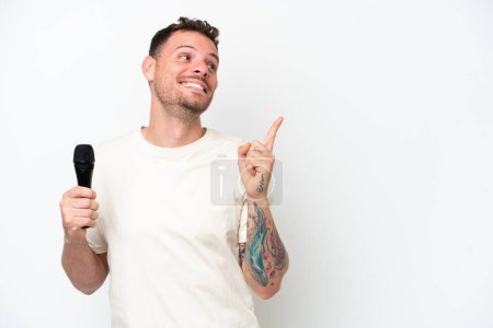 Téléchargez les photos : Jeune chanteur caucasien ramasser un microphone isolé sur fond blanc dans l'intention de réaliser la solution tout en levant le doigt - en image libre de droit