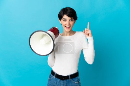 Foto de Mujer con el pelo corto aislado sobre fondo azul sosteniendo un megáfono y señalando una gran idea - Imagen libre de derechos