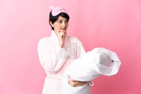 Téléchargez les photos : Femme aux cheveux courts isolé sur fond rose en pyjama et tenant un oreiller tout en pensant - en image libre de droit
