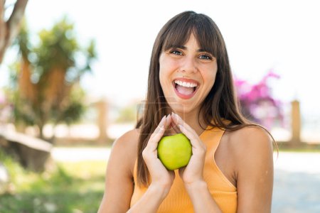 Photo for Young woman at outdoors holding an apple with surprised expression - Royalty Free Image