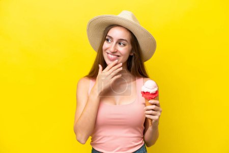 Foto de Joven caucásico con un helado de corneta aislado sobre fondo amarillo mirando hacia arriba mientras sonríe - Imagen libre de derechos