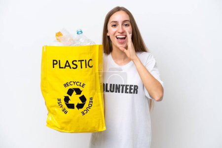Young caucasian woman holding a bag full of plastic bottles to recycle isolated on white background shouting with mouth wide open