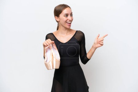 Foto de Mujer joven caucásica practicando ballet aislado sobre fondo blanco apuntando con el dedo hacia un lado y presentando un producto - Imagen libre de derechos