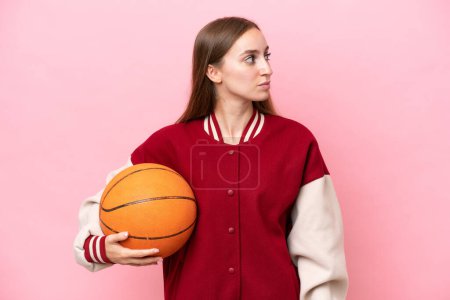 Téléchargez les photos : Jeune joueur de basket-ball caucasien femme sur fond rose isolé regardant sur le côté - en image libre de droit