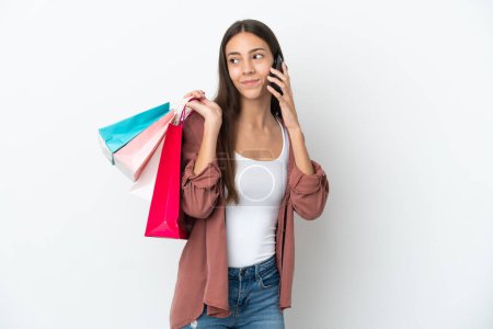 Foto de Joven francesa aislada sobre fondo blanco sosteniendo bolsas de compras y llamando a un amigo con su teléfono celular - Imagen libre de derechos