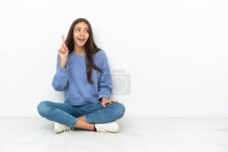 Photo for Young French girl sitting on the floor intending to realizes the solution while lifting a finger up - Royalty Free Image