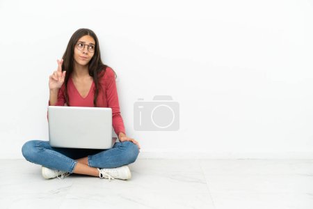 Foto de Joven francesa sentada en el suelo con su portátil con los dedos cruzando y deseando lo mejor - Imagen libre de derechos