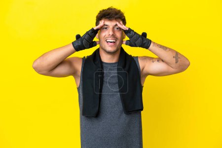 Téléchargez les photos : Jeune homme caucasien sportif avec serviette isolée sur fond jaune avec expression surprise - en image libre de droit