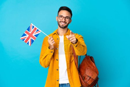 Téléchargez les photos : Jeune homme caucasien tenant un drapeau du Royaume-Uni isolé sur fond jaune surpris et pointant devant - en image libre de droit