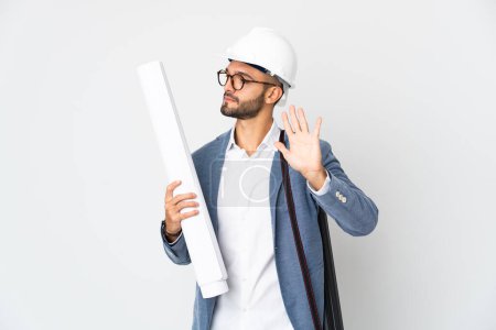 Photo for Young architect man with helmet and holding blueprints isolated on white background making stop gesture and disappointed - Royalty Free Image