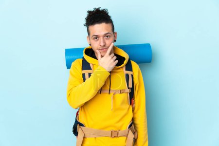 Photo for Young mountaineer man with a big backpack over isolated blue background thinking an idea - Royalty Free Image
