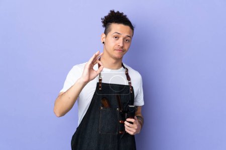 Barber man in an apron over isolated purple background showing an ok sign with fingers