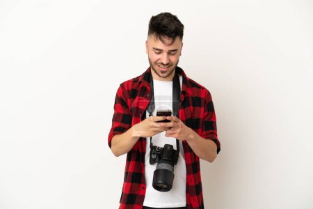 Téléchargez les photos : Jeune photographe caucasien isolé sur fond blanc envoyant un message avec le mobile - en image libre de droit