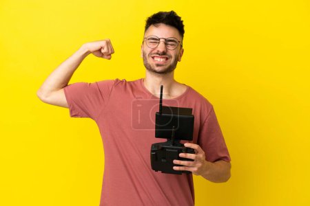 Man holding a drone remote control isolated on yellow background doing strong gesture