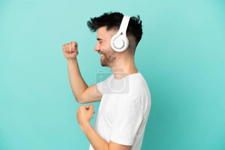 Young caucasian man isolated on blue background listening music and dancing