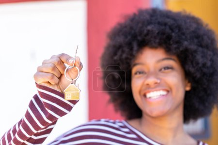 Téléchargez les photos : Afro-américaine fille à l'extérieur tenant les clés de la maison avec expression heureuse - en image libre de droit
