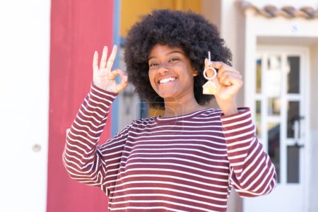 Foto de Chica afroamericana sosteniendo las llaves del hogar al aire libre mostrando ok signo con los dedos - Imagen libre de derechos