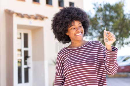 Foto de Chica afroamericana sosteniendo las llaves del hogar al aire libre con expresión feliz - Imagen libre de derechos