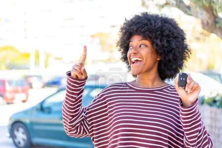 Foto de Chica afroamericana sosteniendo las llaves del coche al aire libre con la intención de realizar la solución mientras levanta un dedo - Imagen libre de derechos