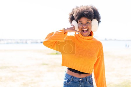 Téléchargez les photos : Afro-américaine fille portant des manchons d'hiver à l'extérieur faisant geste de téléphone. Rappelle-moi signe - en image libre de droit