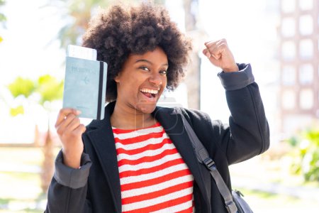 Photo for African American girl at outdoors holding a passport and celebrating a victory - Royalty Free Image